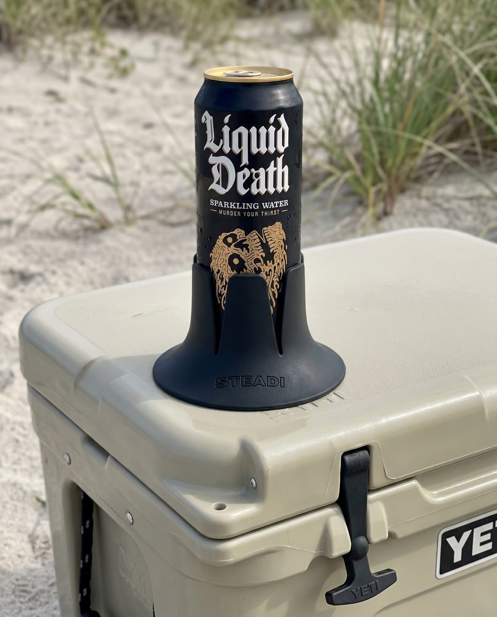 A tall can standing in a black Steadi on the lid of a cooler, outdoors.