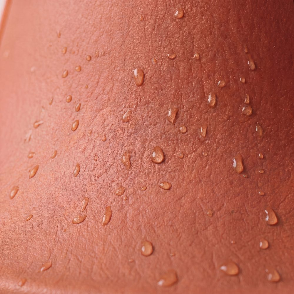 A macro photograph of the matte surface of a terracotta Steadi with water droplets on it.